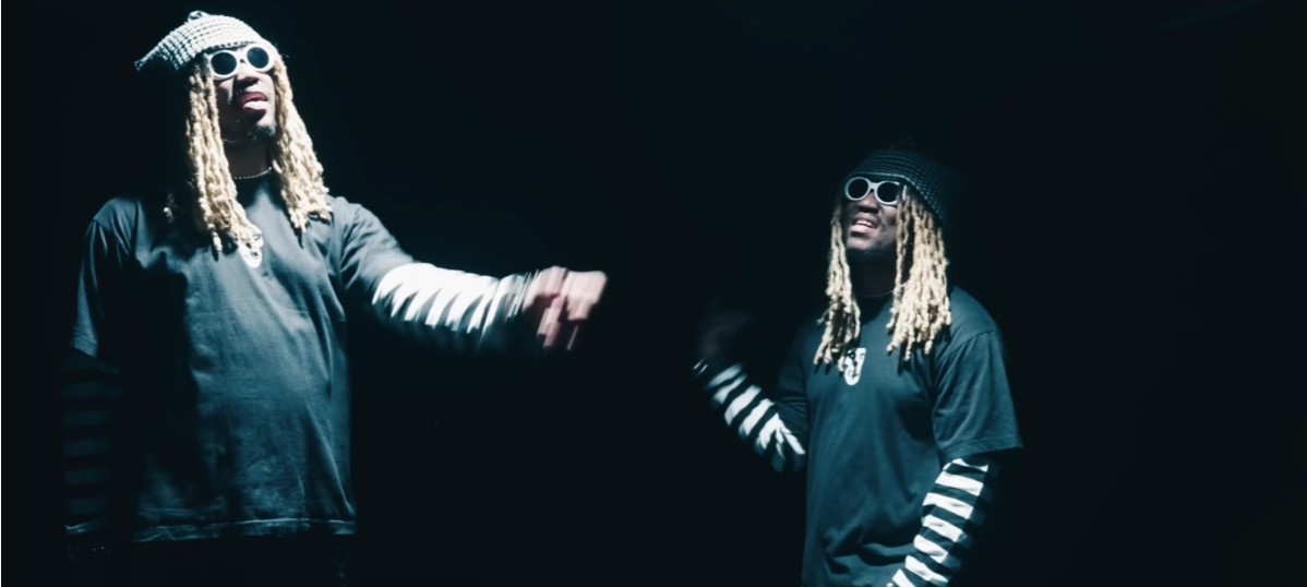 Two music artists performing against a dark background